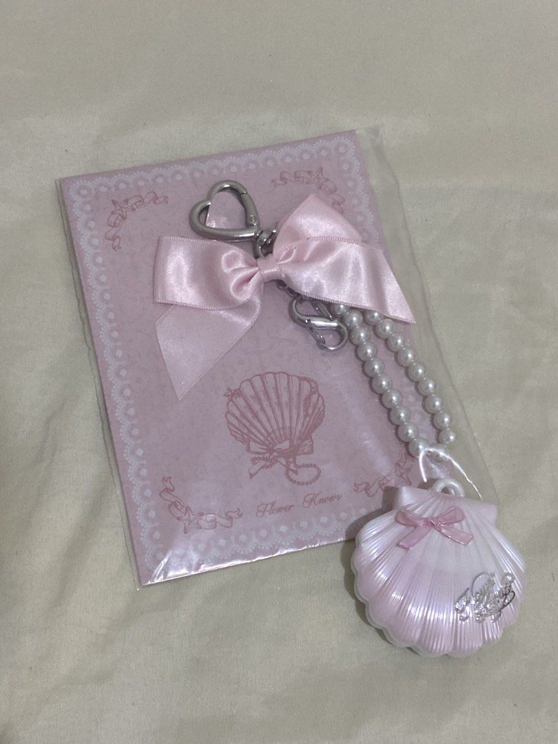 Flower Knows Shell Compact Keychain Set Pink (Category: Makeup) located in Manila. Submitted by lexaa.908 (Listing ID 1447547011, Image 2). Description: - Adorable pink shell-shaped compact with a pearlescent finish and a cute pink bow. - Matching keychain with a delicate pearl strap and a charming heart-shaped clasp. - Both items proudly display the Flower Knows logo. - Ideal for makeup enthusiasts or as a thoughtful gift..