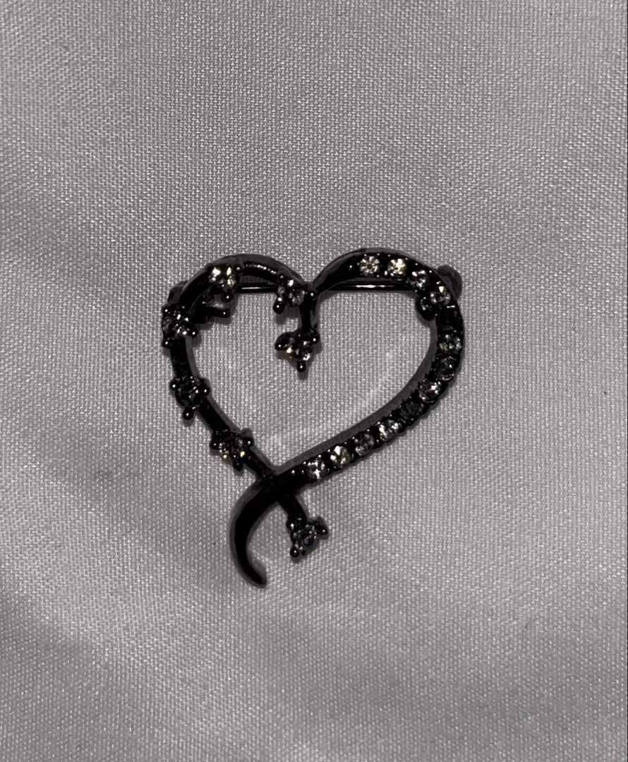 Heart Shaped Brooch with Rhinestones (Category: Brooches) located in Tabuk. Submitted by zenwolf-1867 (Listing ID 1447664257, Image 1). Description: - Cute heart-shaped brooch - Dark metal finish - Adorned with small clear rhinestones - Ribbon-like element wraps around the heart - Secure pin closure on the back - Adds a lovely sparkle to any outfit.