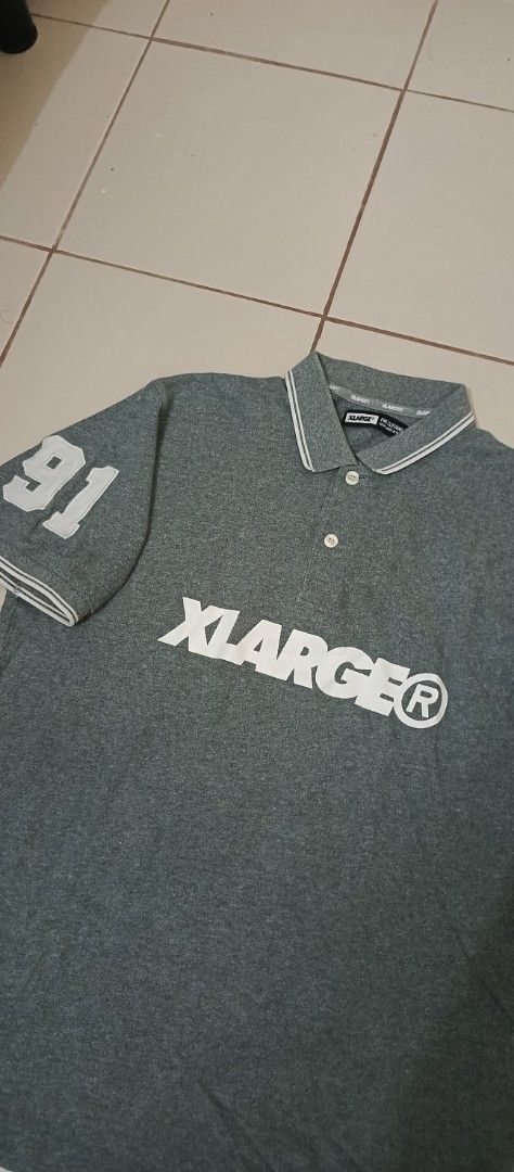 XLARGE® 91 Graphic Polo Shirt Grey (Category: Tshirts & Polo Shirts ) located in Santa Cruz. Submitted by jm.stuffs (Listing ID 1447636780, Image 2). Description: - XLARGE® Polo Shirt in XL size. - Features iconic XLARGE® logo on the front. - '91' graphic detail on the sleeve. - Stylish striped collar and sleeve cuffs. - Small red XLARGE® trademark tag on the hem. - Perfect for a cool, casual look..