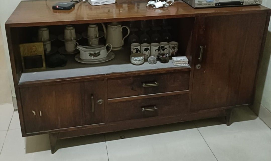 Bufet Pendek Jati Jengki (Vintage 1970an) (Kategori: Perabotan Rumah) berada di Bogor. Dikirim oleh rinirachma68263 (ID iklan 1447821582, Gambar 1). Deskripsi: Bufet pendek bermodel retro/jengki dengan kaki meruncing khas era mid-century. Memiliki kompartemen terbuka untuk pajangan, dua laci di tengah, serta pintu lemari di sisi kiri dan kanan. Terbuat dari kayu jati tua (est. 1970an) yang sangat kokoh, tahan rayap, dan memiliki nilai historis/kl