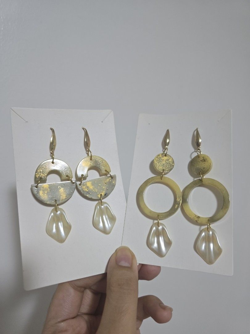 BUNDLE OF 2: Gold Tone Statement Earrings with Pearl Dangles (Category: Earrings) located in Pasig City. Submitted by callmemaf (Listing ID 1447681319, Image 1). Description: - Set of 2 unique gold tone earrings. - One pair features circular and pointed charms. - The other pair has half-circle charms with textured gold accents. - Both pairs have creamy, shell-shaped pearl dangles. - Ideal for dressing up any outfit. - gold plated ss316.