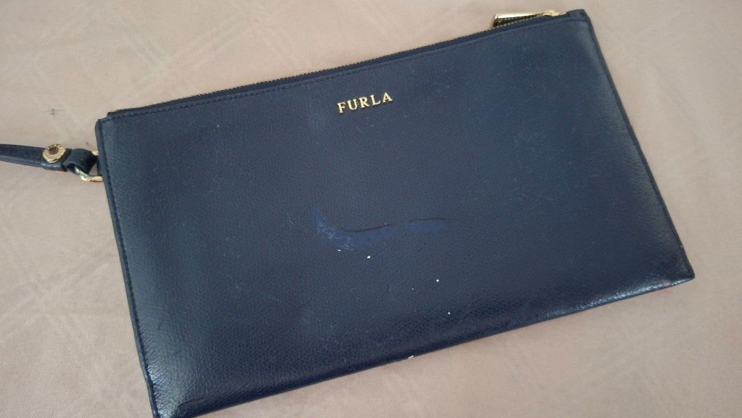 Furla Navy Leather Clutch Bag (Category: Luxury Bags & Wallets) located in Pasay City. Submitted by chaserstar (Listing ID 1447728830, Image 1). Description: Authentic Navy blue leather clutch from Furla. Zip closure with wrist strap. Some marks and scuffs on the exterior, shown in photos. Leather is slightly sticky due to storage. Interior is clean. Great for essentials and for repainting. Original is priced at around $150. Super steal!.