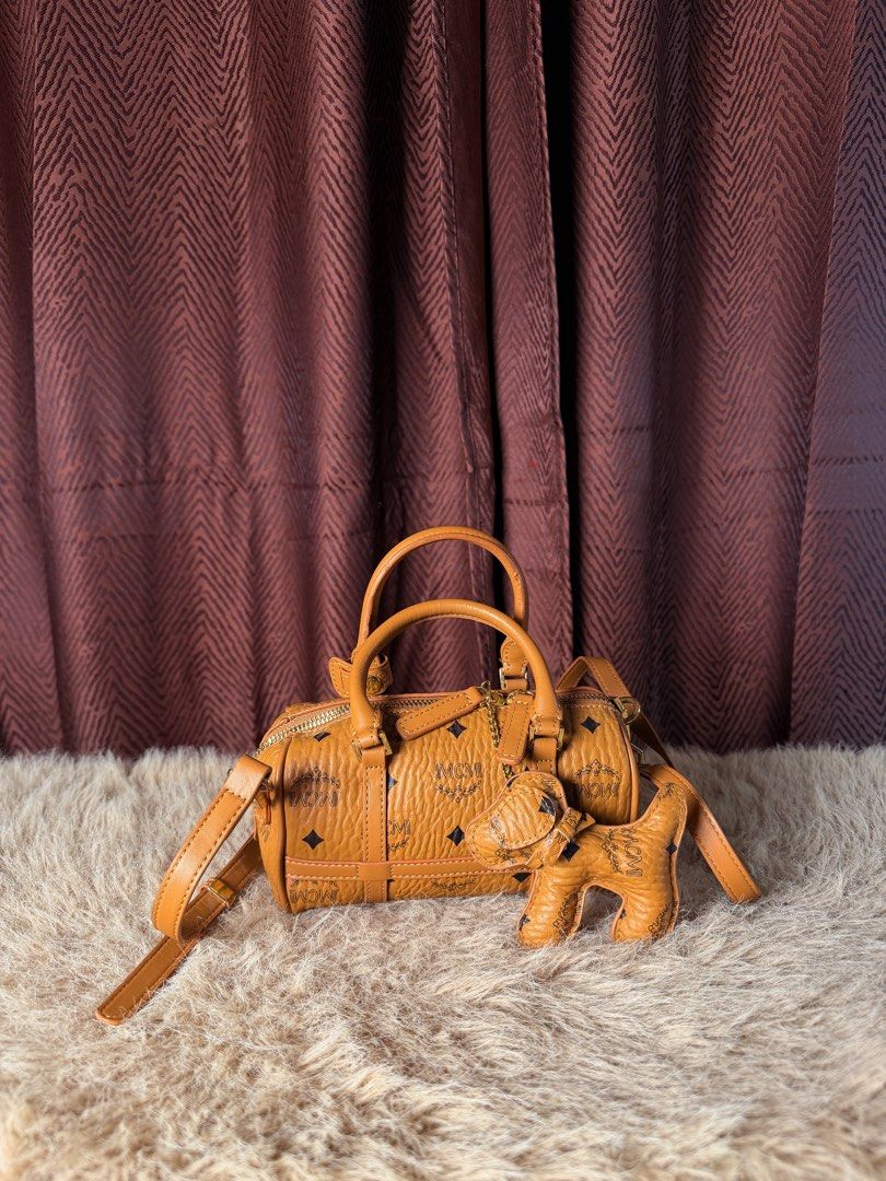 MCM Monogram Barrel Bag with Dog Charm (Category: Luxury Bags & Wallets) located in Manila. Submitted by femnlofficial (Listing ID 1447881777, Image 1). Description: - Cute MCM barrel bag in signature monogram print - Comes with a matching dog charm - Features top handles - Includes a detachable crossbody strap - Great for everyday use or weekend trips - Nice textured leather - Easy zip opening.