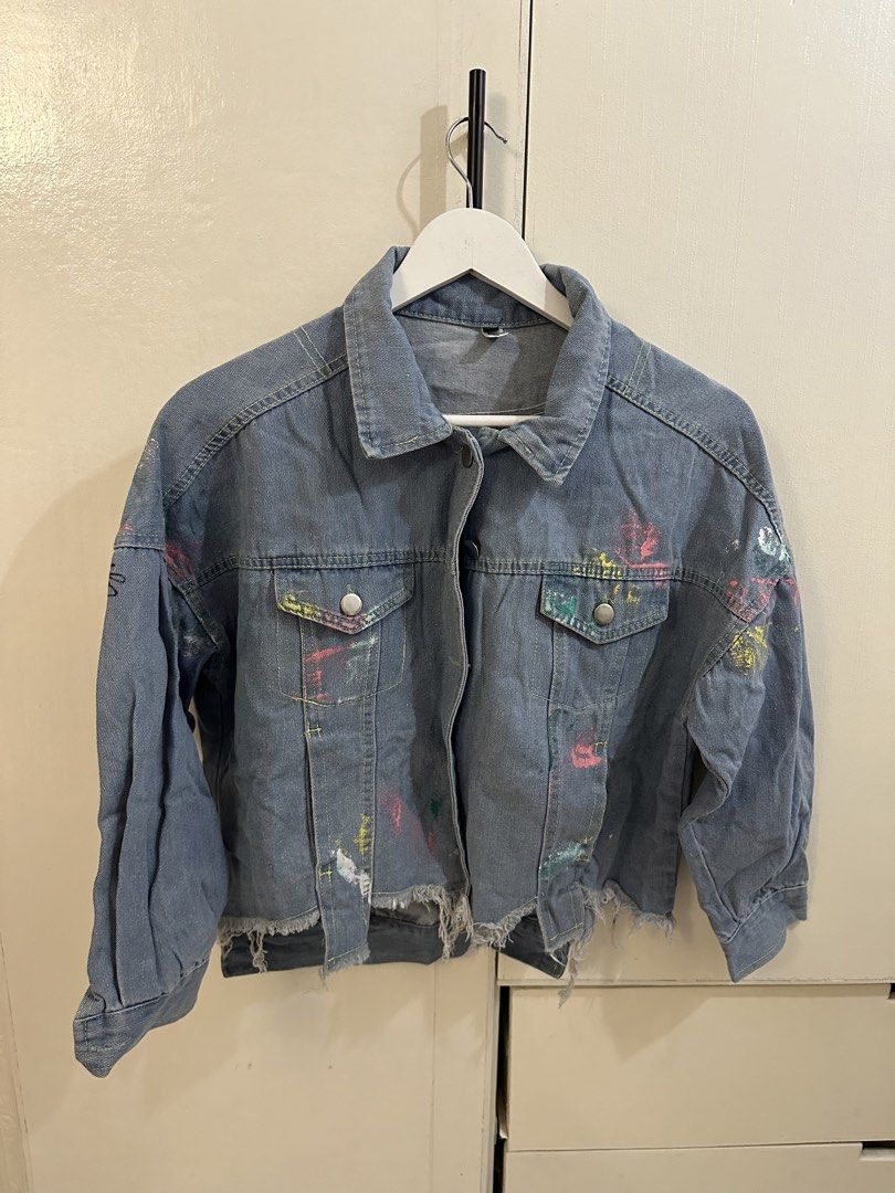 Mila Distressed Denim Jacket with Paint Splatter and Graffiti (Category: Coats, Jackets and Outerwear) located in Pasig City. Submitted by gwi0mi (Listing ID 1447874143, Image 1). Description: Brand: Mila Size: L Length: 22.9in Width: 22.5in Sleeve length: 28.5in Style: Denim Jacket Features: Distressed hem and cuffs Design: Colorful paint splatters all over Back Detail: Graffiti-style writing Condition: 10/10 No flaws Unique, great for layering.