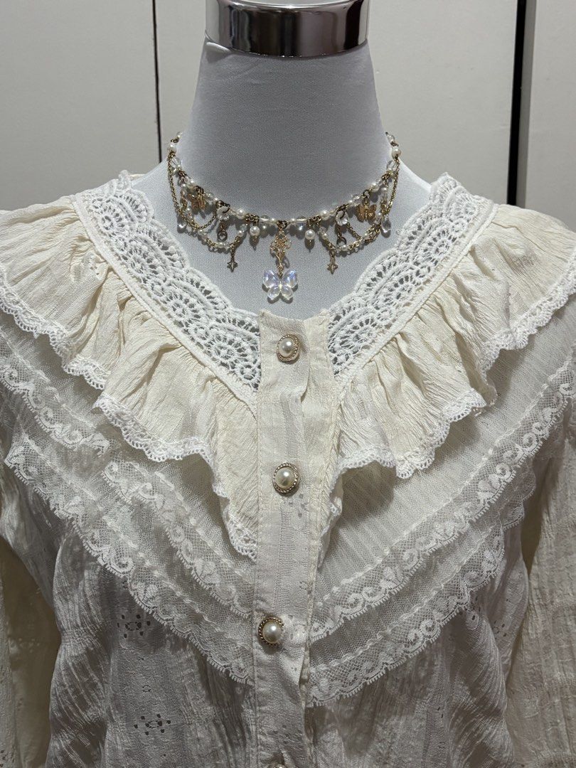 (m-l) White Lace Ruffle Long Sleeve Blouse (Category: Blouses) located in Paranaque City. Submitted by prelovedtinez (Listing ID 1448042393, Image 2). Description: - Cream white blouse with intricate lace details - Features ruffles along the neckline and sleeves - Button-up front with pearl-like buttons - Textured fabric with eyelet details - Long sleeves with ruffled cuffs - Delicate and vintage-inspired design.