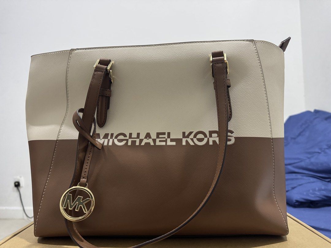 Original Michael Kors Tote Bag - Beige and Brown (Category: Tote Bags) located in Kuala Lumpur. Submitted by haslizahairani (Listing ID 1448212831, Image 2). Description: - Michael Kors tote bag - Stylish two-tone design: Beige and Brown - Iconic MK logo printed on the front - Includes a charming hanging MK logo accessory - Durable leather handles and trim - Spacious interior, ideal for everyday essentials.