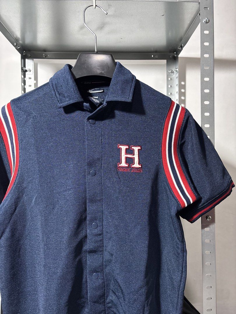 Tommy Hilfiger Short Sleeve Polo (Category: Activewear) located in Santa Rosa. Submitted by popeye00 (Listing ID 1448086486, Image 2). Description: - Navy blue short sleeve polo shirt from Tommy Jeans. - Medium, 24L 18W - Features iconic 'H' logo on the chest. - 'HILFIGER' branding across the back. - Sporty red and white stripe details on the sleeves..