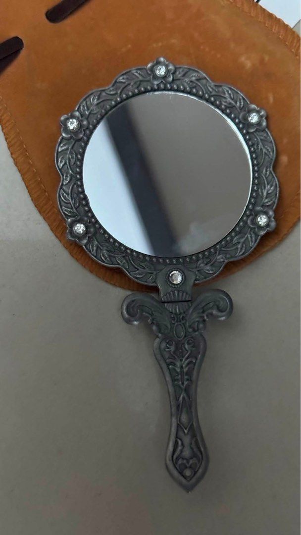 Vintage Folding Vanity Mirror - Ornate Silver Tone Frame (Category: Mirrors) located in Mandaluyong City. Submitted by elainelawenko (Listing ID 1448186970, Image 2). Description: - 5" handheld folding vanity mirror - Vintage style with ornate silver-tone frame - Red backing with floral painted design and embedded crystals - Includes a brown pouch - Ideal for travel or display.