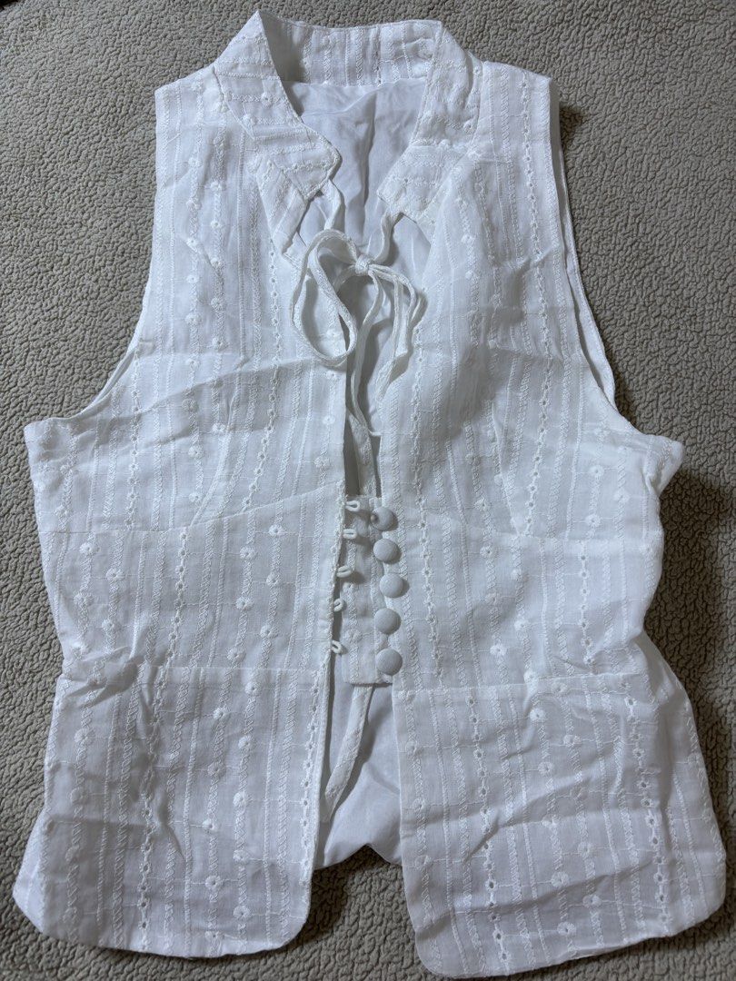 White Broderie Anglaise Vest with Tie Front (Category: Sleeveless) located in Makati City. Submitted by skelssei (Listing ID 1448165692, Image 2). Description: - White sleeveless vest - Features delicate broderie anglaise with floral patterns - Vertical stripe detailing - Tie front closure with button details down the front - Classic collar neckline - Estimated size: Small to Medium - Ideal for stylish layering.