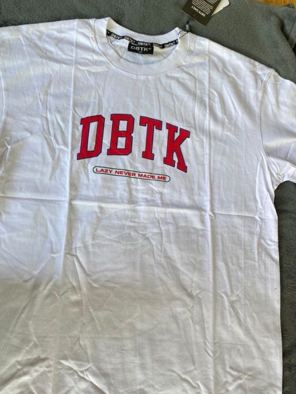 DBTK "Don't Blame The Kids" (Category: Tshirts & Polo Shirts ) located in Porac. Submitted by declutteringwtnics (Listing ID 1448318096, Image 2). Description: - White DBTK graphic t-shirt - Features multiple 'DBTK' logos - 'Don't Blame The Kids' text prominently displayed - 'Lazy Never Made Me' text at the bottom - Makes a bold statement piece - Check the tag for specific details.