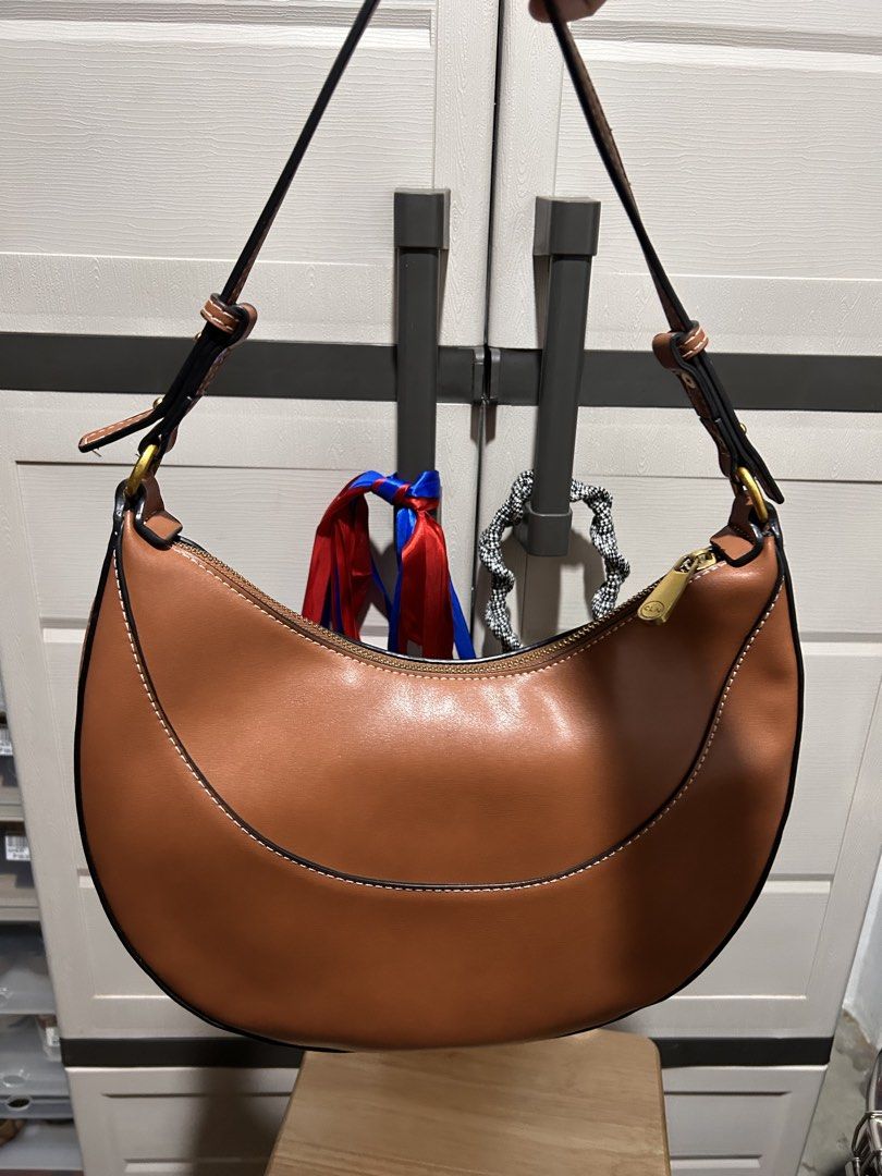 Brown Crescent Shoulder Bag with Scarf Accent (Category: Shoulder Bags) located in Manila. Submitted by mariamaxi41499 (Listing ID 1448554991, Image 2). Description: - Chic brown shoulder bag with a stylish crescent shape. - Elegant stitched detailing along the edges. - Interior lining features a repeating logo pattern. - Adorned with a colorful scarf tied to the strap. - Accented with gold-tone hardware on the zipper and strap rings. - Includes 