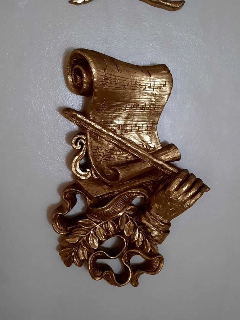 Gold Wall Decor - Floral Branch and Scroll with Hands (Category: Wall Decor) located in Manila. Submitted by epictree.a37e8d (Listing ID 1448642365, Image 2). Description: - Set of two elegant gold-colored wall decor pieces. - Piece 1: Delicate floral branch with numerous small flowers and leaves. - Piece 2: Classical scroll design featuring musical notes, a rolled edge, hands holding a staff, and a laurel wreath. - Ideal for creating a vintage o