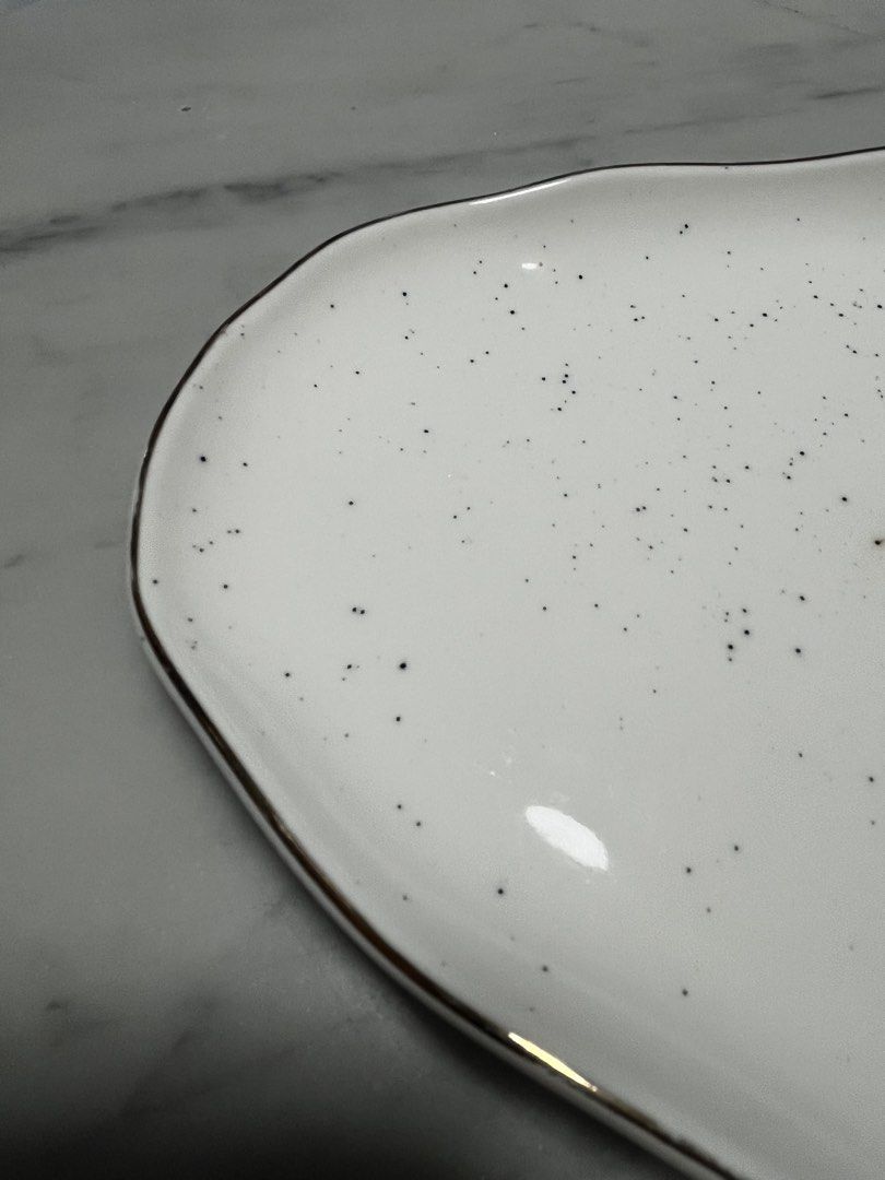 Serving Platter (Category: Dinnerware & Cutlery) located in Singapore. Submitted by design.shopping (Listing ID 1453053797, Image 2). Description: - White speckled serving platter (36cm) - Unique irregular shape - Thin gold rim detail - Brand new - Ideal for appetizers, snacks, or small dishes - Adds a unique touch to any table setting - Suitable for parties and everyday use.
