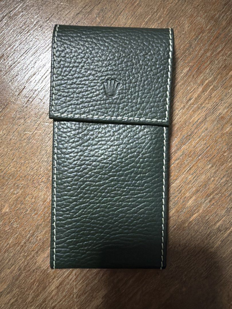 Rolex Pouch (Category: Accessories) located in Singapore. Submitted by belgiumgollie (Listing ID 1454893639, Image 1). Description: - Genuine Rolex pouch - Color: Deep forest green - Material: Textured leather - Design: Classic flap with embossed Rolex crown - Features: White contrast stitching, secure snap closure - Condition: Excellent, brand new - Ideal for storing and protecting your Rolex watch.