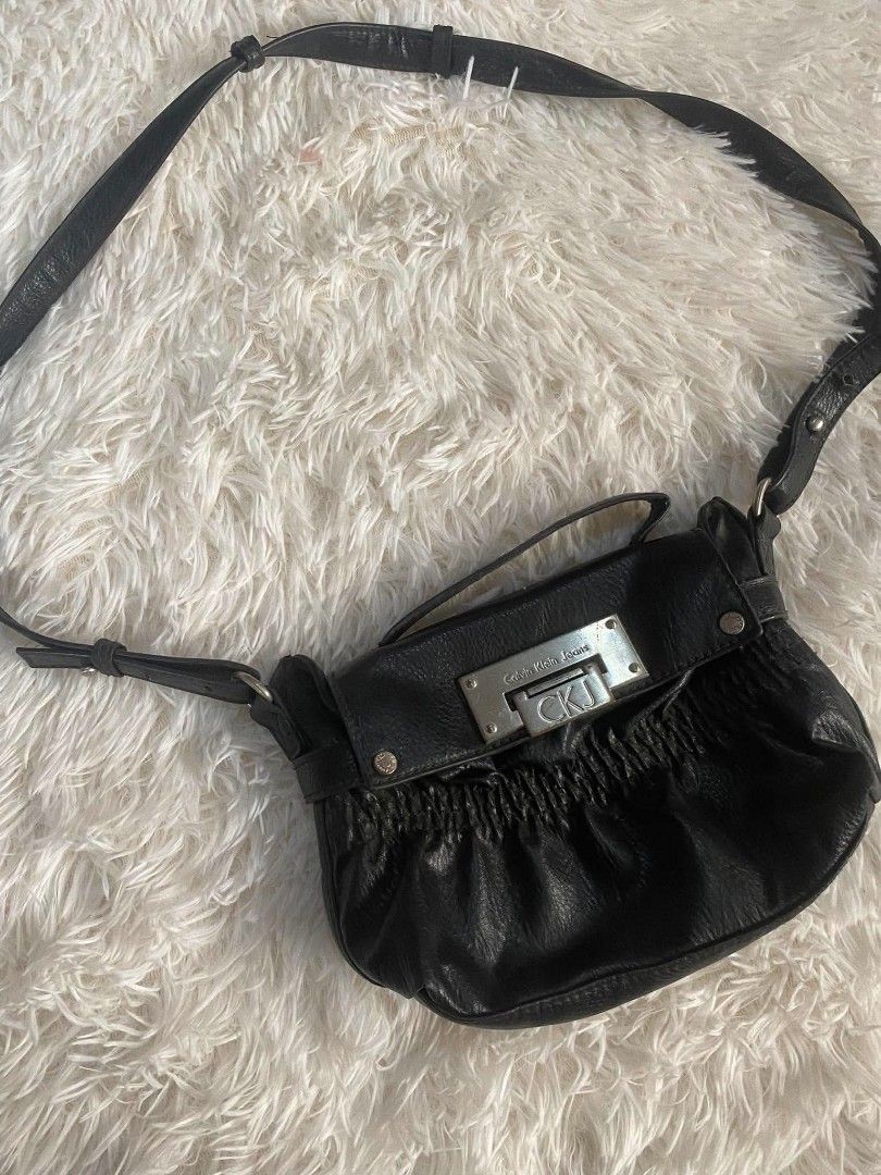 Calvin Klein Jeans Black Leather Shoulder Bag (Category: Shoulder Bags) located in Manila. Submitted by thritingera25 (Listing ID 1455136436, Image 2). Description: Black leather shoulder bag from Calvin Klein Jeans. Features a silver CK buckle closure. Ruched detailing on the front. Adjustable strap. Great for everyday use. Shows some signs of wear on the leather and strap..
