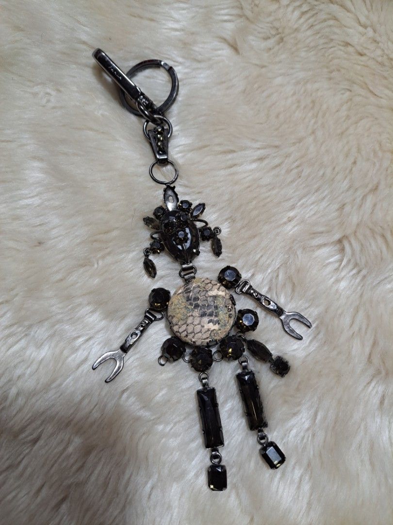 Prada Embellished Keychain with Spanner and Gemstones (Category: Luxury Accessories) located in Quezon City. Submitted by sbvdmanaog (Listing ID 1455030058, Image 1). Description: - Unique keychain with a cool design. - Features a central circular piece with a snake-like pattern. - Adorned with black gemstones and small spanner charms. - Clip has the embossed Prada logo. - Great accessory for your bag or keys. **some parts missing but still funct