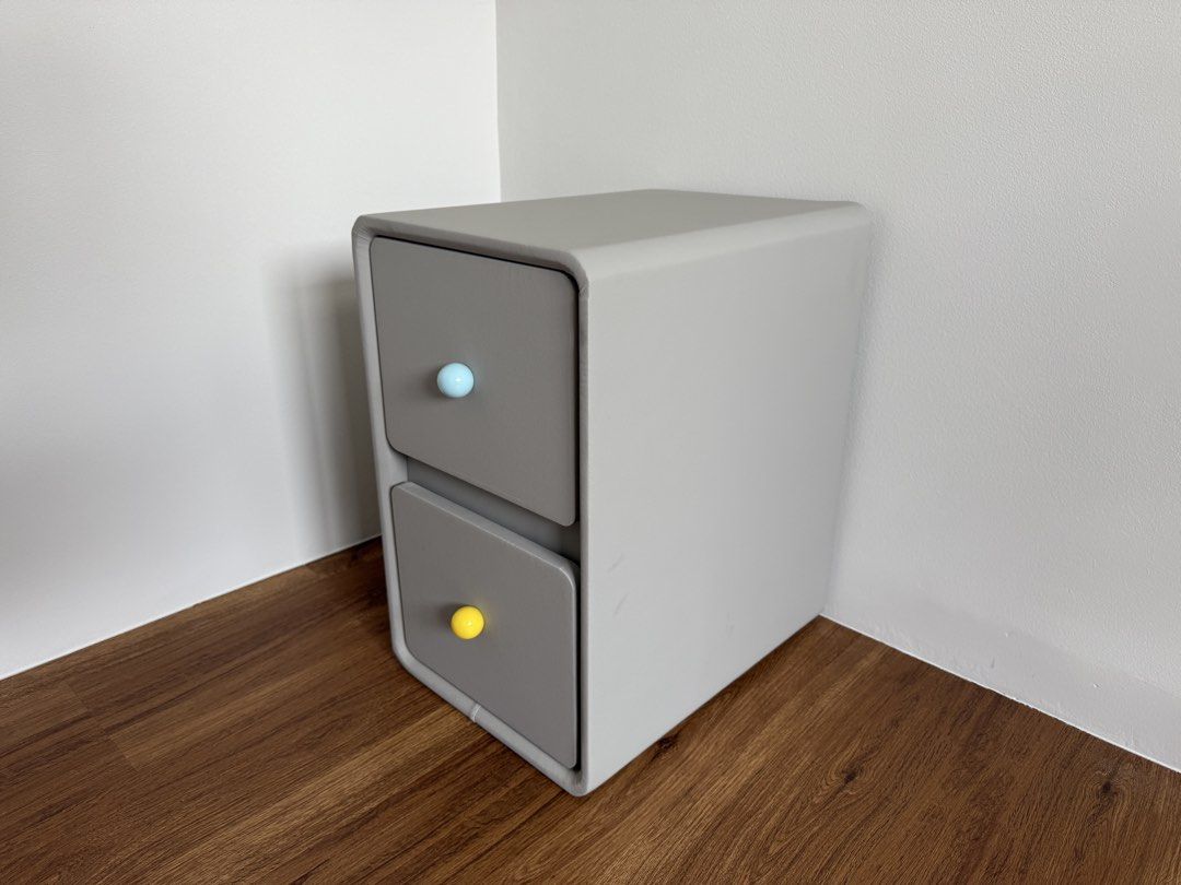 Grey 2-Drawer Bedside Table with Interchangeable Knobs (Category: Tables & Sets) located in Singapore. Submitted by jellypoop (Listing ID 1455146055, Image 1). Description: - Grey bedside table - Two smooth-gliding drawers - Comes with a set of colorful knobs (blue, yellow, pink, red, white) for customization - Dimensions: 47cm (Height) x 40cm (Width) x 30cm (Length).