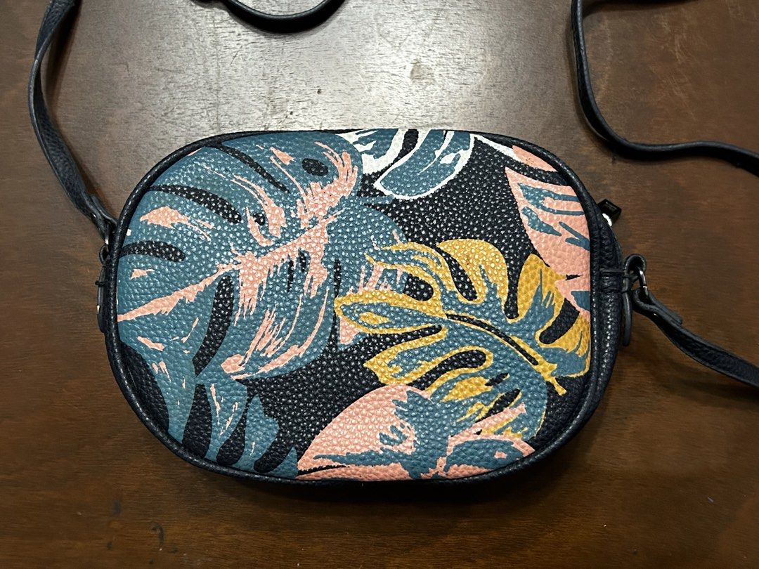 MANGO Oval Crossbody Bag with Tropical Leaf Print (Category: Cross-body Bags) located in Manila. Submitted by my_krophone (Listing ID 1455205243, Image 2). Description: - Cute oval crossbody bag - Fun tropical leaf print (pink, teal, yellow on black background) - Dark navy strap and trim - Two zippered compartments - Ideal for casual outings or travel.