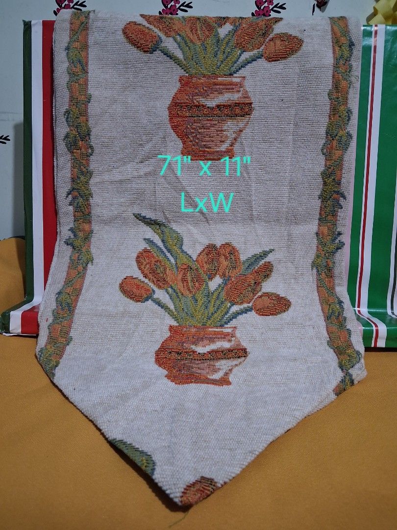 Tulip Tapestry Table Runner 71" x 11" (Category: Table Linen & Textiles) located in Hinigaran. Submitted by faye_fab (Listing ID 1455221911, Image 1). Description: - Cream colored table runner - Features a tapestry design with orange tulips in vases - Border showcases a green and brown vine pattern - Dimensions: 71 inches long x 11 inches wide - Ideal for adding a decorative touch to your dining table or entryway.