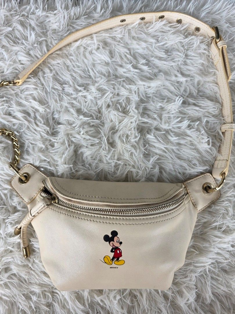 Cream Mickey Mouse Fanny Pack with Gold Chain Strap (Category: Cross-body Bags) located in Lemery. Submitted by venus23 (Listing ID 1455325251, Image 1). Description: - Cream colored fanny pack - Features a cute Mickey Mouse graphic on the front - Zipper closure - Gold chain strap with adjustable buckle - Can be worn as a crossbody or around the waist - Approximate measurements: 7 inches wide x 5 inches tall.
