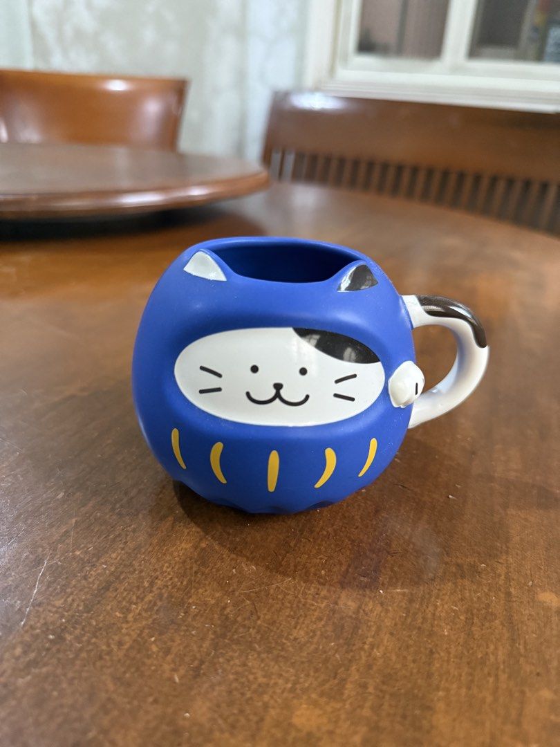 Starbucks Blue Daruma Cat Mug (Category: Coffee & Tea Tableware) located in Manila. Submitted by ninisegisss (Listing ID 1455399107, Image 1). Description: - Adorable blue mug shaped like a Daruma doll with a cute cat face. - Features charming yellow stripes at the bottom. - Equipped with a stylish black and white handle. - Ideal for enjoying your morning coffee or tea. - A perfect gift for collectors or any cat lover. - Adds a fun and unique tou