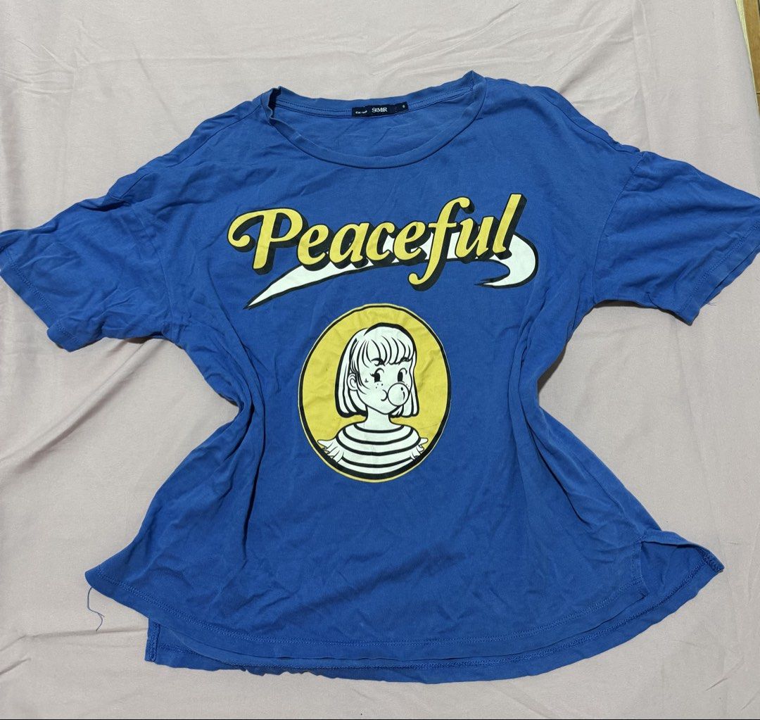Blue Graphic T-shirt (Category: Shirts) located in Muntinlupa City. Submitted by sunwonx (Listing ID 1455607641, Image 1). Description: - Blue graphic t-shirt - Features 'Peaceful' text print and a cute cartoon character - Short sleeves and round neckline - Made from soft and comfortable fabric - Ideal for casual wear - Easily pairs with jeans or shorts.