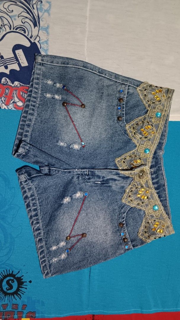 Customized Denim Shorts with Lace and Embellishments (Category: Shorts) located in Pasay City. Submitted by keenfox.a73ed0 (Listing ID 1455509587, Image 1). Description: - Unique blue denim shorts - Gold lace and blue bead embellishments on waistband - Red stitching detail on front pockets - Distressed look with small rips - Standard back pockets - Size 27.