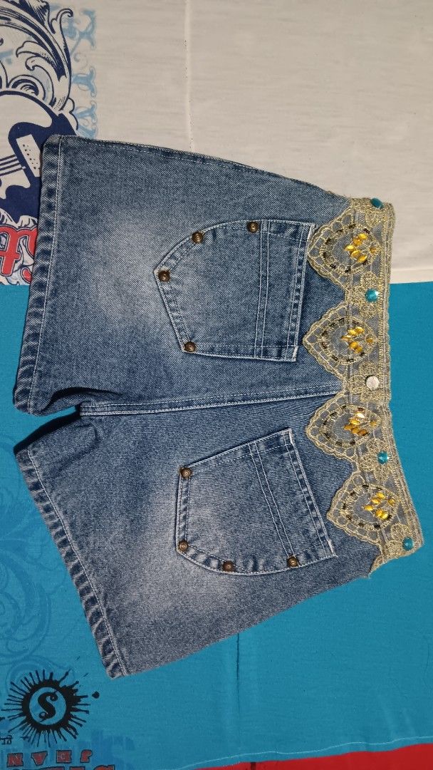 Customized Denim Shorts with Lace and Embellishments (Category: Shorts) located in Pasay City. Submitted by keenfox.a73ed0 (Listing ID 1455509587, Image 2). Description: - Unique blue denim shorts - Gold lace and blue bead embellishments on waistband - Red stitching detail on front pockets - Distressed look with small rips - Standard back pockets - Size 27.