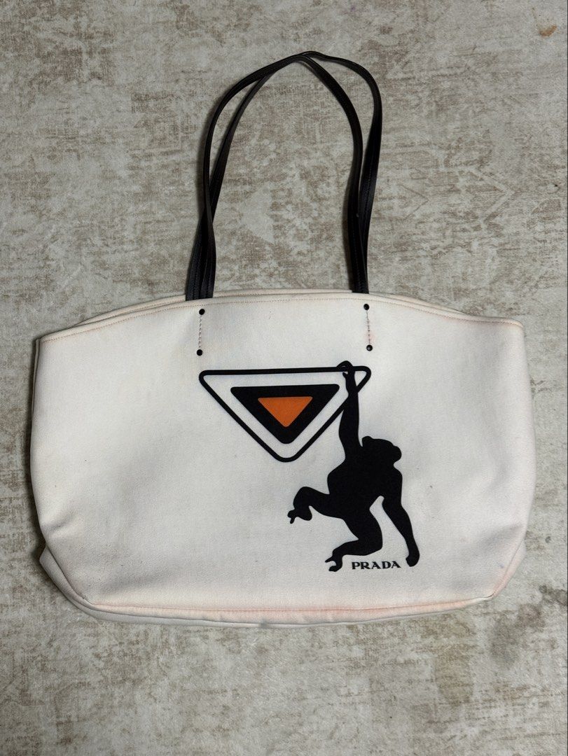 Prada White Canvas Tote Bag with Monkey Graphic (Category: Luxury Bags & Wallets) located in Tarlac. Submitted by jemserrano (Listing ID 1455563581, Image 3). Description: - Authentic Prada white canvas tote bag - Features a unique black monkey graphic on the iconic Prada triangle logo - Durable black leather handles - Ideal for everyday errands or weekend getaways Very good condition, need wash, missing inner pouch. Bag only no other inclusions.