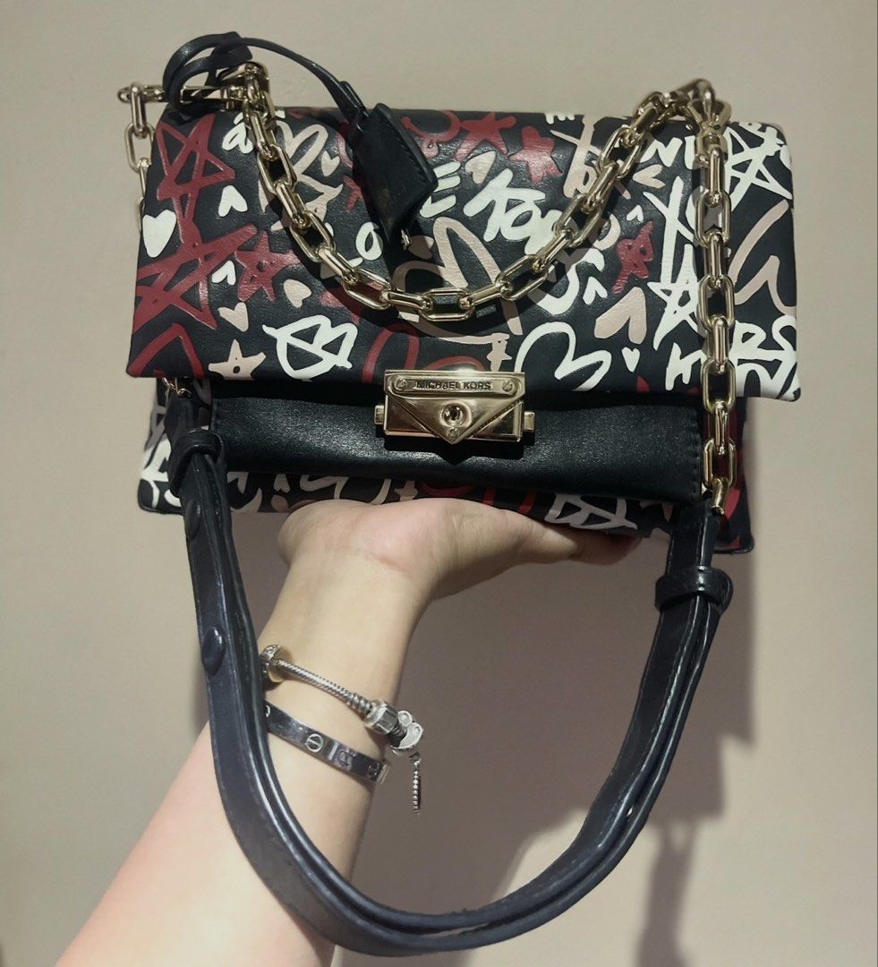 Michael Kors Graffiti Print Leather Shoulder Bag (Category: Luxury Bags & Wallets) located in Trece Martires City. Submitted by justprelovedx (Listing ID 1455697235, Image 1). Description: - Authentic Michael Kors bag - Unique graffiti print design - Black leather with vibrant red, white, and pink accents - Luxurious gold chain strap and hardware - Secure and stylish turn-lock closure - Perfect for adding a statement piece to your look.