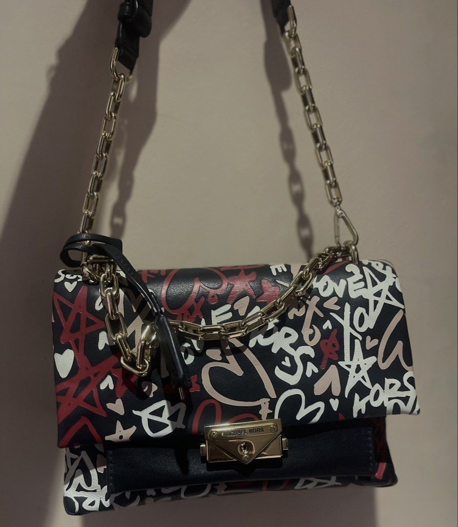 Michael Kors Graffiti Print Leather Shoulder Bag (Category: Luxury Bags & Wallets) located in Trece Martires City. Submitted by justprelovedx (Listing ID 1455697235, Image 3). Description: - Authentic Michael Kors bag - Unique graffiti print design - Black leather with vibrant red, white, and pink accents - Luxurious gold chain strap and hardware - Secure and stylish turn-lock closure - Perfect for adding a statement piece to your look.