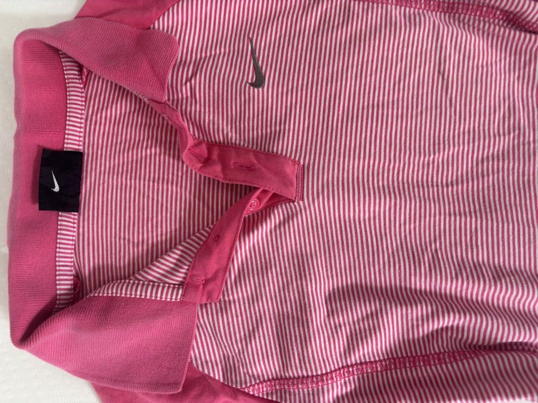 Nike Pink Striped Polo Shirt (Category: Activewear) located in Binan City. Submitted by byhiraeth (Listing ID 1455791936, Image 2). Description: - Pink and white striped Nike polo shirt - Solid pink shoulders and collar - Short sleeves - Button-up neckline - Small Nike swoosh logo on chest - Ideal for sports or casual wear - Comfortable and breathable fabric.