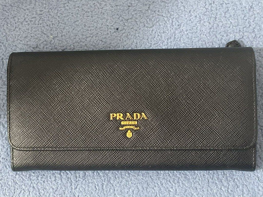 Prada Saffiano Leather Continental Flap Wallet (Category: Luxury Bags & Wallets) located in Manila. Submitted by alldayshoppinggirl (Listing ID 1455870261, Image 1). Description: Prada Saffiano Leather Continental Flap Wallet in black with gold-tone hardware lettering. Material: Crafted from Prada’s signature scratch-resistant cross-hatch embossed Saffiano calf leather. Design: Features a foldover flap with a press-stud snap closure and the iconi