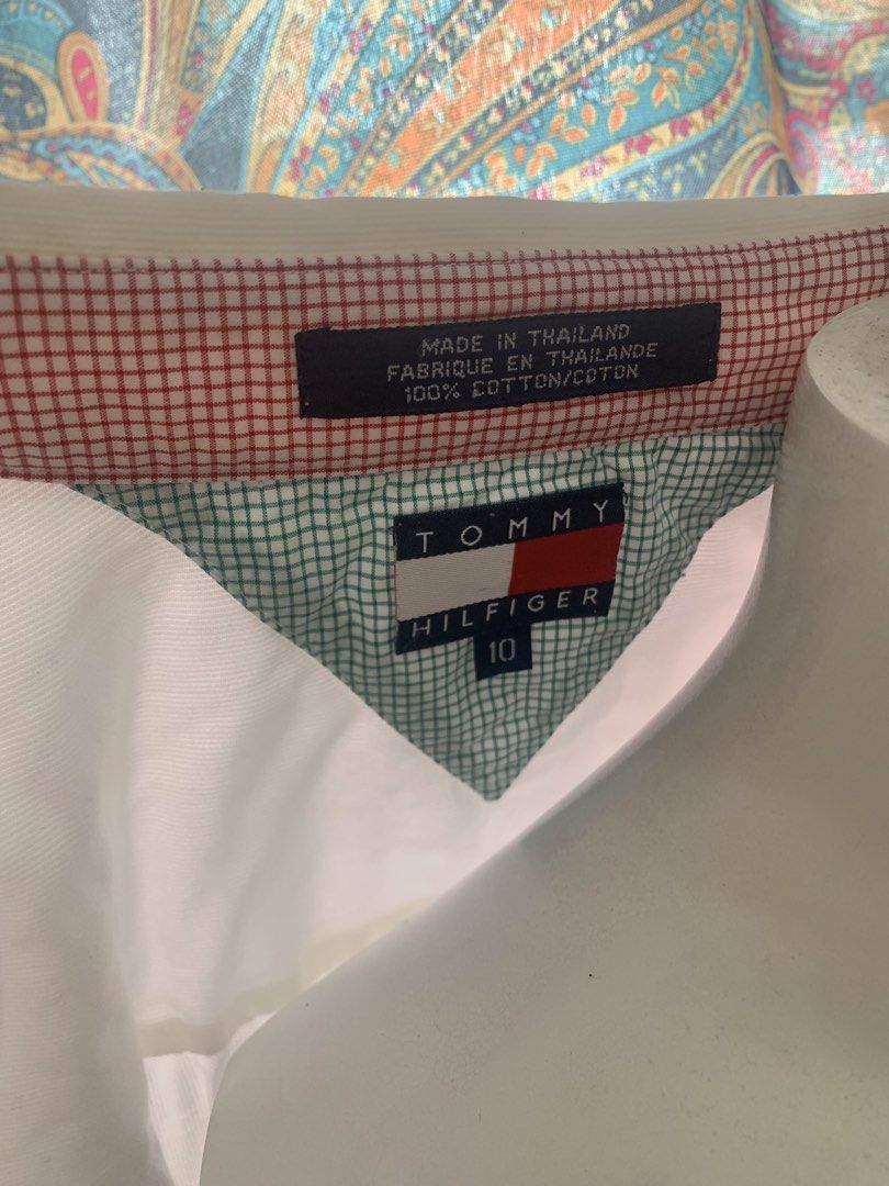 Tommy Hilfiger White Button-Up Shirt Size 10 (Category: Coats, Jackets and Outerwear) located in Manila. Submitted by closetsunday (Listing ID 1455903963, Image 1). Description: - Brand: Tommy Hilfiger - Color: White - Material: 100% Cotton - Origin: Made in Thailand - Size: 10 - Features: Classic collar with red & white checkered trim, chest pocket with embroidered Tommy Hilfiger flag logo.