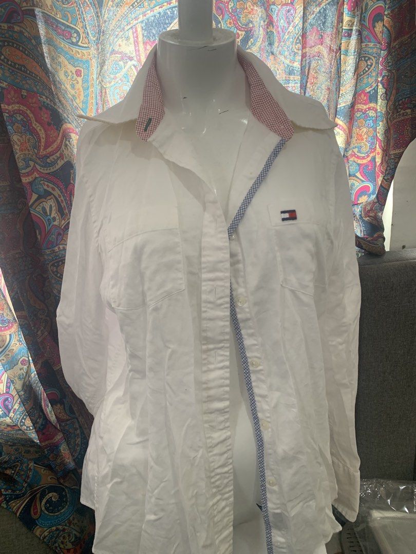 Tommy Hilfiger White Button-Up Shirt Size 10 (Category: Coats, Jackets and Outerwear) located in Manila. Submitted by closetsunday (Listing ID 1455903963, Image 2). Description: - Brand: Tommy Hilfiger - Color: White - Material: 100% Cotton - Origin: Made in Thailand - Size: 10 - Features: Classic collar with red & white checkered trim, chest pocket with embroidered Tommy Hilfiger flag logo.