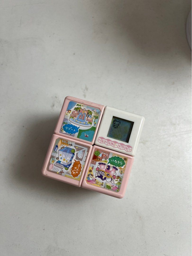 🎲WanTame Hapi Hapi Cube Town (Category: Interactive Toys) located in Tarlac. Submitted by just_decluttering (Listing ID 1455915192, Image 1). Description: 🎲ORIGINAL PRICE: ₱4,549.53 -w/o box -Release by Takara Tomi - Adorable Tamagotchi cube toy - Features a black and white screen - Offers various game screens and characters - Comes in a pink casing with colorful illustrations - Ideal for collectors and fans of retro digital pets.