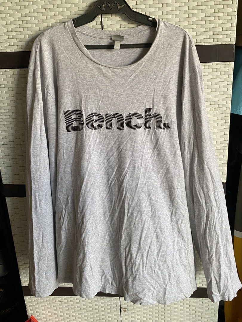 Bench Classic Logo Long Sleeve Shirt (Category: Coats, Jackets and Outerwear) located in Imus. Submitted by curataa (Listing ID 1456187219, Image 2). Description: Bench Classic Logo Long Sleeve Shirt (Heather Grey) •Size: XXL (2XL) / TTG • Condition: Pre-owned / Good used condition • Features: Soft heather grey lightweight cotton fabric with a bold black striped "Bench." chest graphic and classic crewneck collar. • Flaws & Issues: Heavy fabric wr