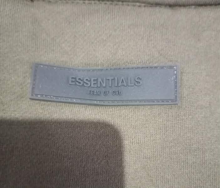 Fear of God Essentials Track Jacket (Category: Coats, Jackets and Outerwear) located in Lapu Lapu. Submitted by mysticwhale.cdda54 (Listing ID 1456175304, Image 3). Description: - Olive green track jacket from Essentials - Full zip closure with stand-up collar - Ribbed cuffs and hem for a snug fit - "ESSENTIALS FEAR OF GOD" logo prominently displayed on the back - Comfortable and stylish, ideal for layering.
