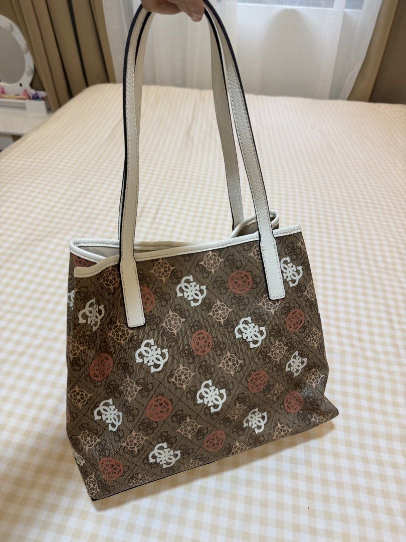 Guess Vicky II Tote Bag (Category: Luxury Bags & Wallets) located in Las Pinas. Submitted by babyandmommapreloved (Listing ID 1456202655, Image 2). Description: - Guess brown monogram tote bag - White trim and handles - Interior features repeating Guess logo pattern - Comes with a matching small zippered pouch - Ideal for everyday use.