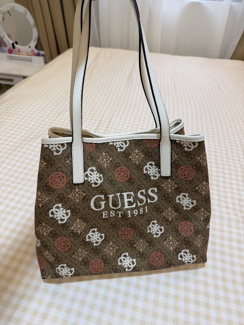 Guess Vicky II Tote Bag (Category: Luxury Bags & Wallets) located in Las Pinas. Submitted by babyandmommapreloved (Listing ID 1456202655, Image 1). Description: - Guess brown monogram tote bag - White trim and handles - Interior features repeating Guess logo pattern - Comes with a matching small zippered pouch - Ideal for everyday use.