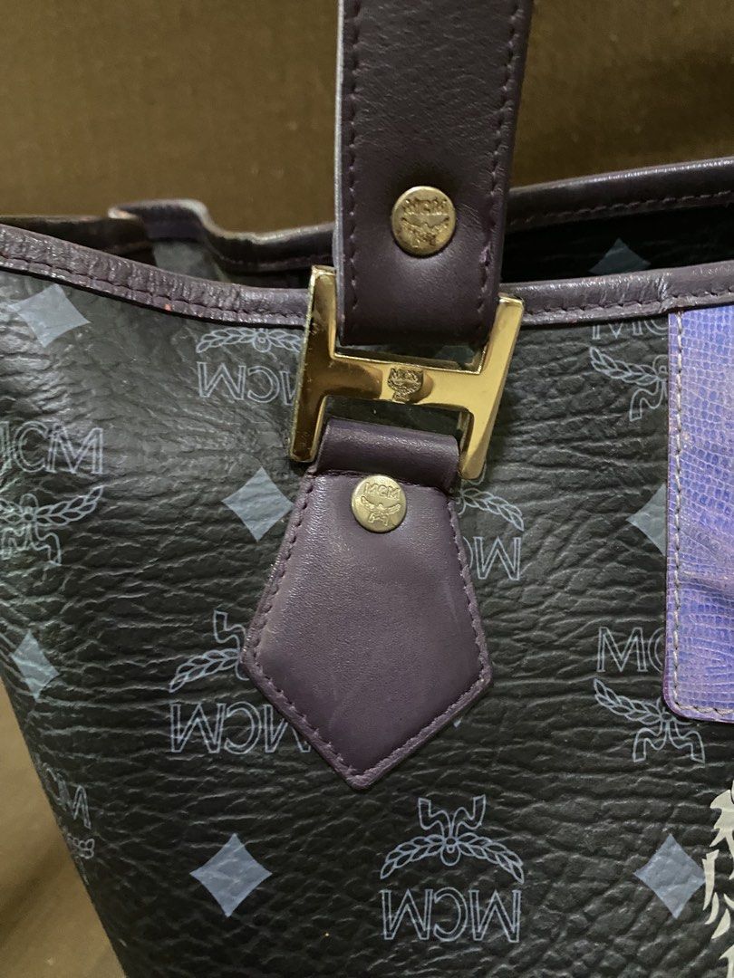 MCM Tote Bag with Lion Emblem (Category: Luxury Bags & Wallets) located in San Antonio. Submitted by pixiechromzzz (Listing ID 1456128110, Image 2). Description: - Authentic MCM tote bag in black with signature pattern. - Features a striking central lion emblem. - Adorned with colorful stripes above and below the emblem. - Elegant purple leather trim and handles. - Polished gold hardware details. - Spacious interior, ideal for everyday use..