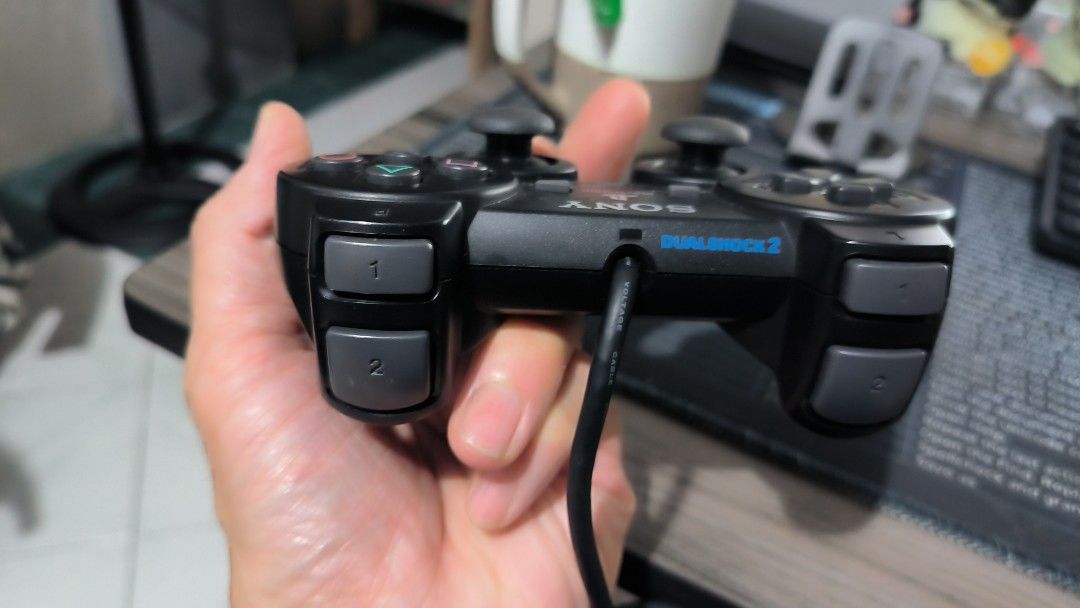 Sony PS2 Dual Shock 2 Controller (Category: Controllers) located in Bulacan. Submitted by tripledouble532 (Listing ID 1456092958, Image 3). Description: For vintage collection: Classic black Sony PlayStation 2 DualShock 2 Controller featuring twin analog sticks, a directional pad, and standard action buttons. [1] Type: Wired analog controller with force-feedback vibration Compatibility: Designed primarily for the PlayStation 2 and backward compat