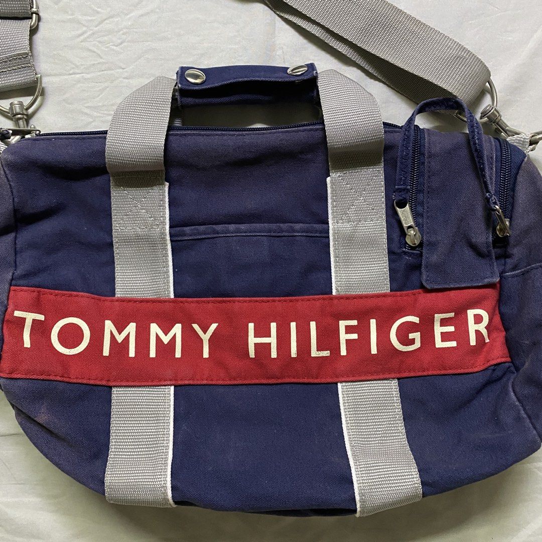 Tommy Hilfiger Navy Blue Duffle Bag with Shoulder Strap (Category: Shoulder Bags) located in Marikina City. Submitted by beeeekenneth (Listing ID 1456140868, Image 2). Description: - Navy blue Tommy Hilfiger duffel bag - Signature red and white logo band on front - Top handles and detachable shoulder strap - Zipped main compartment - Front zip pocket - Small side pockets - Ideal for gym or weekend trips -sunfade issue Location: Marikina + we can 