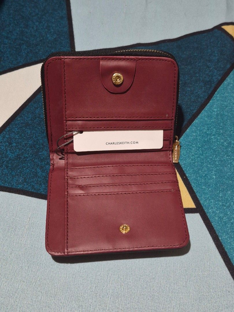 Charles & Keith Black Tri-fold Wallet (Category: Wallets & Card holders) located in Davao. Submitted by wangcollections (Listing ID 1456336224, Image 2). Description: - Brand: Charles & Keith (not guaranteed og) - Color: Black exterior, Burgundy interior - Style: Tri-fold wallet - Features: Card slots, coin pocket - Closure: Zipper - Ideal for: Everyday use.