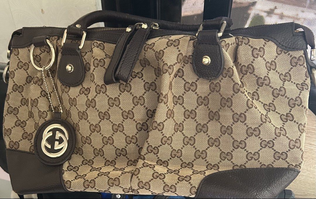 (RUSH! w/o charm) Gucci Sukey Hand Bag (Category: Luxury Bags & Wallets) located in San Jose del Monte. Submitted by declutteriri (Listing ID 1456296046, Image 2). Description: Material: GG canvas body with dark brown cowhide/calfskin leather trim and rolled leather top handles. Hardware: Polished light gold-tone or brass hardware. Signature Charm: Features the iconic interlocking G logo charm dangling from a ring on the front..