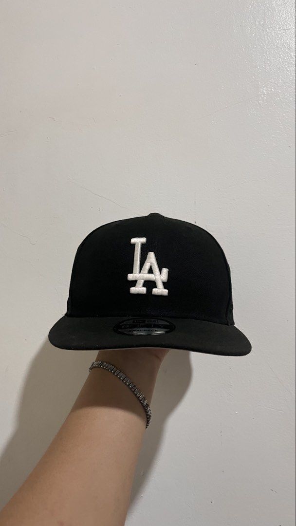 New Era 9Fifty Los Angeles Dodgers Snapback Cap (Category: Caps & Hats) located in Dinalupihan. Submitted by banditvaultco (Listing ID 1456285495, Image 1). Description: Color Scheme: Deep matte black crown, visor, and top button. Front Detail: High-density, raised 3D embroidery of the iconic interlocking white “LA” logo. Left Side: The signature white embroidered New Era flag. Right Side: A special circular monochrome patch for the “Los Angeles 