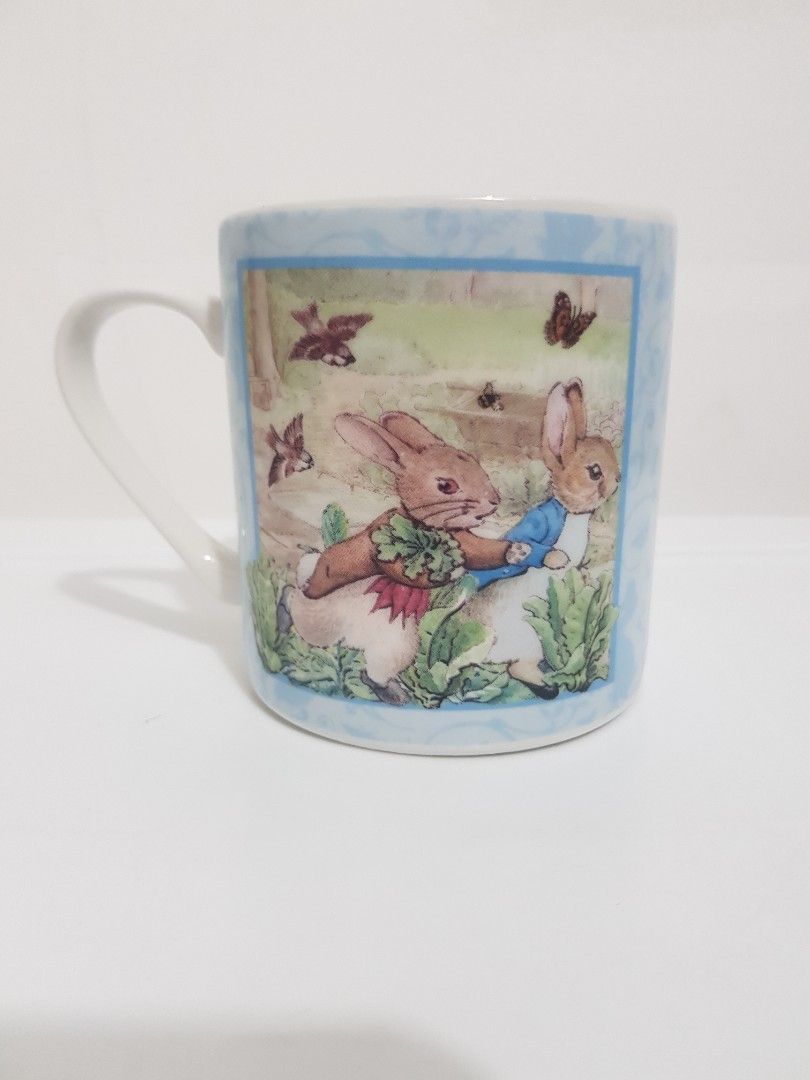 Queens Peter Rabbit Mug by Frederick Warne & Co (Category: Coffee & Tea Tableware) located in Manila. Submitted by salvacionp40231 (Listing ID 1456351029, Image 2). Description: - Adorable Peter Rabbit mug by Queens. - Features illustrations of Peter and friends in a garden. - Licensed by Frederick Warne & Co. - White interior with a light blue patterned border. - Ideal for enjoying your morning coffee or tea..