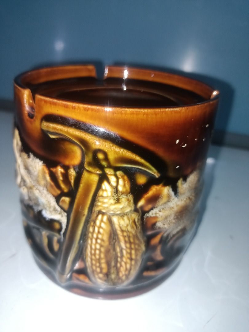 Vintage Ceramic Ashtray with Pickaxe and Corn Design (Category: Dinnerware & Cutlery) located in Munoz. Submitted by larryc1212 (Listing ID 1456336951, Image 3). Description: - Cool vintage ceramic ashtray - Unique design featuring a pickaxe and corn - Brown glaze with textured details - Has slots for cigarettes - Measures approximately 4.25 inches tall - Great for collectors or as a quirky decor item Disclaimer: Item may include some scratches d