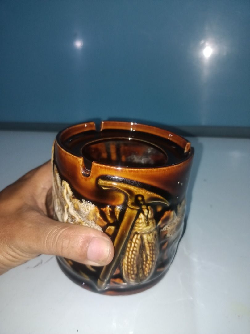 Vintage Ceramic Ashtray with Pickaxe and Corn Design (Category: Dinnerware & Cutlery) located in Munoz. Submitted by larryc1212 (Listing ID 1456336951, Image 2). Description: - Cool vintage ceramic ashtray - Unique design featuring a pickaxe and corn - Brown glaze with textured details - Has slots for cigarettes - Measures approximately 4.25 inches tall - Great for collectors or as a quirky decor item Disclaimer: Item may include some scratches d