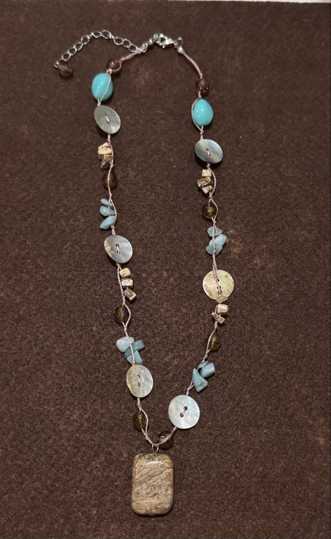 Boho Beaded Necklace with Wood Pendant (Category: Necklaces) located in Quezon City. Submitted by kcapi (Listing ID 1456562752, Image 1). Description: - Handmade necklace with a unique bohemian style. - Features a mix of turquoise, brown, and light blue beads. - Includes charming shell buttons. - Pendant is a rectangular wood with a distinctive pattern. - Adjustable chain with an extender for a perfect fit. - Adds a beautiful bohemian touch to an